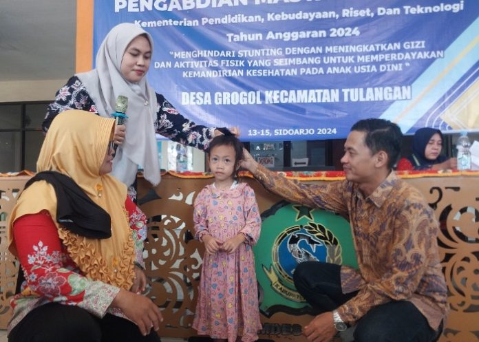 Ketua Pelaksana Pengabdian Masyarakat Unipa Surabaya, Riga Mardhika, S.Pd., M.Or. melihat pengukuran tinggi badan anak di balai Desa Grogol Kecamatan Tulangan Sidoarjo/Foto: Ipung Syaiful