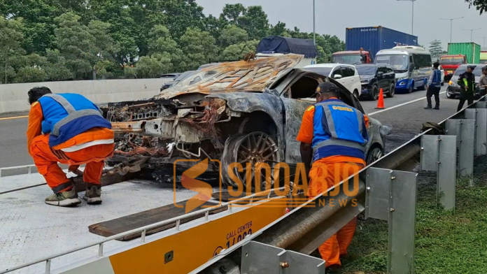 Petugas saat mengevakuasi bangkai mobil sedan yang terbakar/Foto: hnf