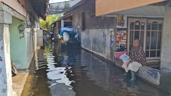 Potret salah satu warga yang duduk didepan rumahnya yang kebanjiran/Foto : istimewa.